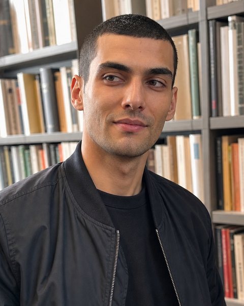 Hayden Ball, with short dark hair and a dark jacket, in a bookshop